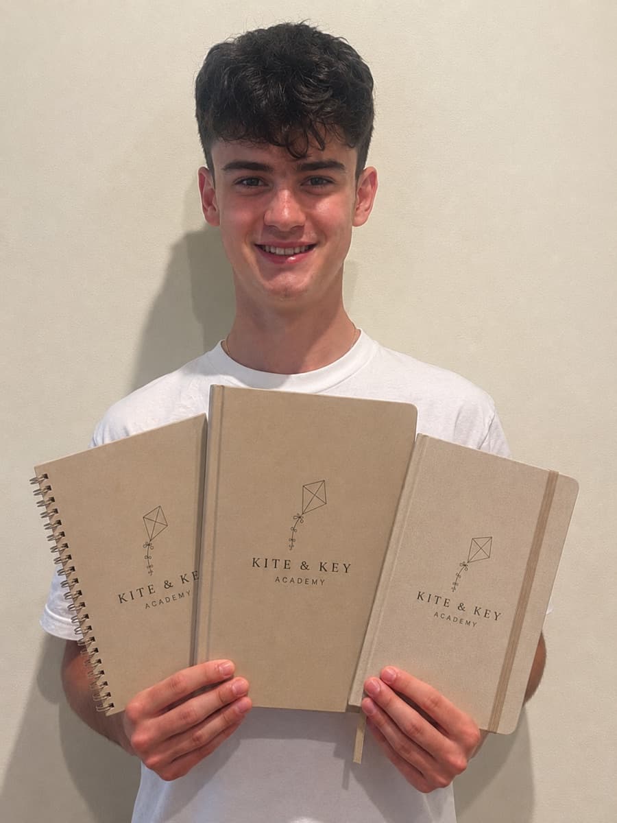 Joshua, one of our students, smiling and holding three Kite & Key Academy notebooks